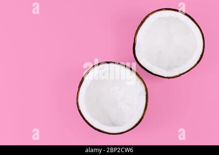 Due metà aperte di frutta di cocco intera su sfondo rosa Foto Stock