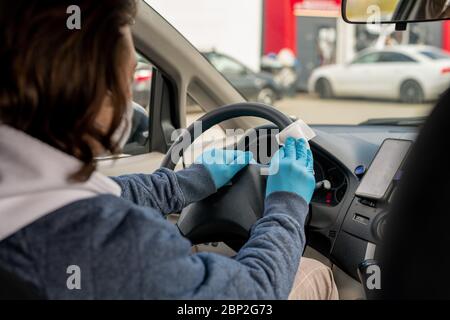 Uomo con guanti di protezione pulizia cruscotto auto con panno in