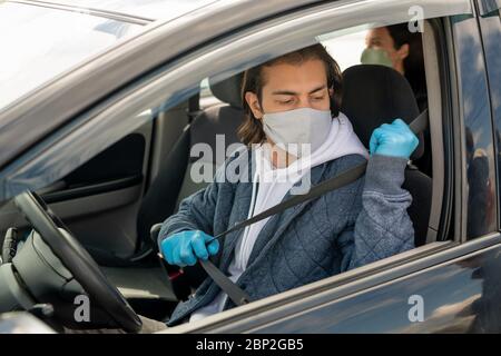 Giovane uomo in felpa con cappuccio, giacca, guanti protettivi e maschera che va a mettere la cintura mentre si siede in auto e andare a casa dopo lo shopping Foto Stock