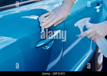 Donna disinfetta la maniglia della porta dell'auto con uno spray antibatterico. Lavaggio auto Foto Stock