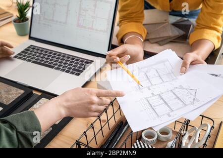 Mani di giovane donna designer o architetto che punta alla carta con il disegno di casa mentre spiegare alcuni dettagli alla collega durante la riunione Foto Stock