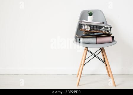 Sedia da ufficio in plastica grigia con campioni di tessuto ripiegati, cesto con forniture, documenti e piccolo vaso da fiore in cima in piedi a parete Foto Stock