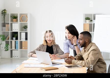 Gruppo di giovani e fiduciosi dirigenti d'ufficio interculturali che si occupano di brainstorming e discutere idee per il loro nuovo progetto o presentazione Foto Stock