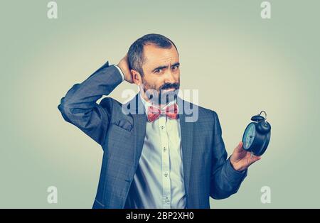 Stressato uomo infastidito con sveglia. E' troppo tardi, presto per quella riunione. Modello bearded misto corsa isolato su sfondo verde studio con Foto Stock