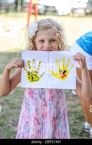 bambina che mostra stampe a mano su carta dipinta con colori brillanti Foto Stock
