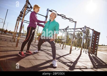 Donna sportiva matura che parla qualcosa al marito mentre si fa sport insieme all'aperto. Felice coppia matura in abbigliamento sportivo che si esercita insieme nel Foto Stock