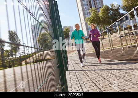 Jog di mattina. Coppia di famiglia matura attiva in abbigliamento sportivo che corre insieme allo stadio la mattina presto. Lunghezza completa. Bella coppia seniour Foto Stock