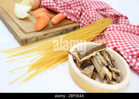 Prodotti alimentari disposti sul tavolo con volant, con quadrati rossi e bianchi. Cucina mediterranea italiana con spaghetti ai funghi porcini secchi. Foto Stock