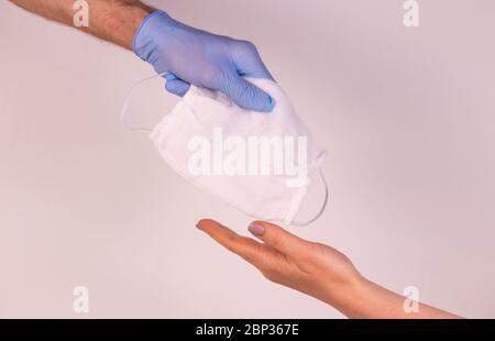 Una mano in un guanto blu dà ad una persona bisognosa una maschera medica. Aiuti umanitari. Il concetto di assistenza virale Foto Stock