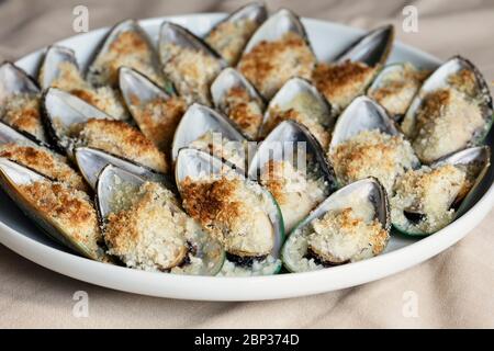 Cozze cotte con parmigiano, pangrattato e burro di erbe servite su un piatto. Cibo di fondo. Cucina mediterranea. Concetto per un gustoso e sano me Foto Stock