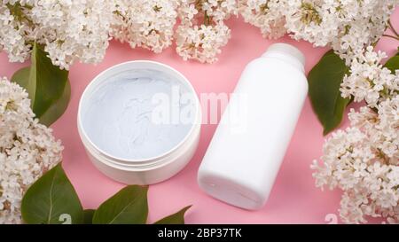 bottiglie bianche con cosmetici per il corpo su sfondo rosa con rami in fiore lilacs primo piano, bellezza, cura della pelle, spa. Foto Stock