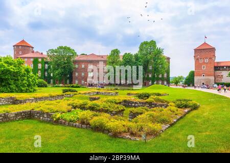 Cracovia, Polonia - 18 giugno 2019: Wawel Royal Castle vista torri colorate contro il letto dei fiori e alberi verdi nel giardino Foto Stock