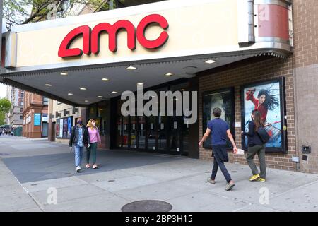 Le persone con maschere facciali camminano davanti ad un teatro chiuso AMC nel lato Upper West di Manhattan, New York durante la crisi del coronavirus COVID-19. Foto Stock