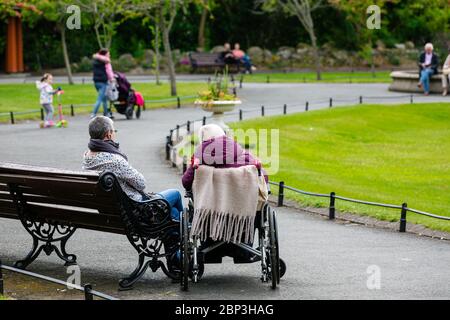 Anziani in sedia a rotelle con tutore seduto accanto a una panchina nel Parco Verde di Santo Stefano`s a Dublino durante il Covid-19 Pandemic Irlanda. Foto Stock