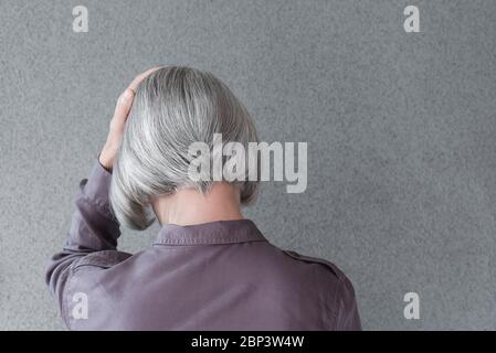 Donna con capelli grigi sconvolto, tenendo la testa con la mano, su sfondo grigio con spazio per la copia. Foto Stock