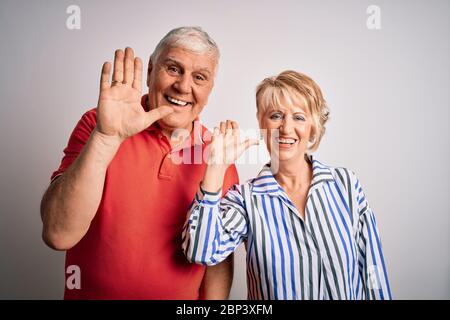 Anziano bella coppia che si erge insieme su isolato sfondo bianco cintura dicendo ciao felice e sorridente, amichevole gesto di benvenuto Foto Stock