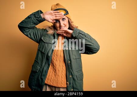 Bella sciatrice bionda di età media indossando abbigliamento sportivo da neve e occhiali da sci sorridente allegro giocando a peek un boo con le mani che mostrano il volto. Sorpreso Foto Stock