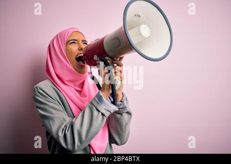 Business arab donna indossare hijab gridando arrabbiato per protesta attraverso il megafono. Urlando eccitato sulla conversazione ludspeaker e urlando le notizie Foto Stock