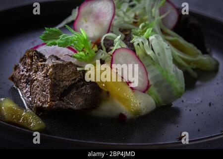Primo piano vista su guancia di manzo smaltata con purea di sedano e pera di zenzero su sfondo grigio nel ristorante Foto Stock