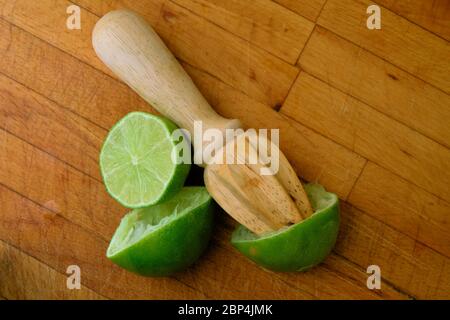 Lime centrifugate tagliate a metà su un tagliere di legno con un alesatore di agrumi; spremute o spremute per la spremitura. Foto Stock