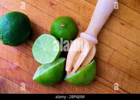 Lime centrifugate tagliate a metà su un tagliere di legno con un alesatore di agrumi; spremute o spremute per la spremitura. Foto Stock