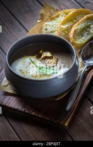 Zuppa di cappuccino con funghi su tagliere di legno. Tre fette di pane bianco e un cucchiaio su sfondo di legno marrone nel ristorante. Verticale Foto Stock