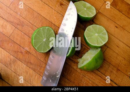 Lime centrifugate tagliate a metà su un tagliere di legno con un coltello; spremute o spremute per la spremitura. Foto Stock