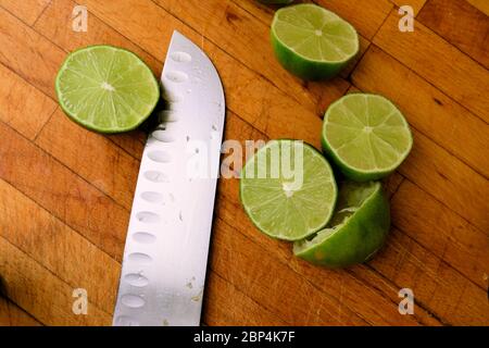 Lime centrifugate tagliate a metà su un tagliere di legno con un coltello; spremute o spremute per la spremitura. Foto Stock