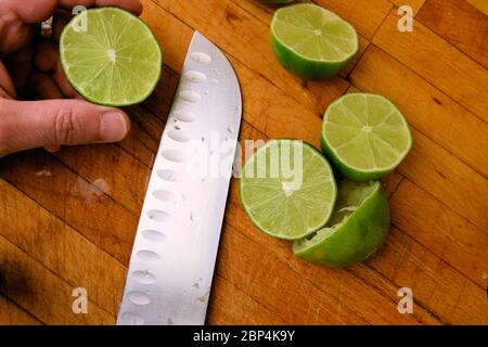 Lime centrifugate tagliate a metà su un tagliere di legno con un coltello; spremute o spremute per la spremitura. Foto Stock