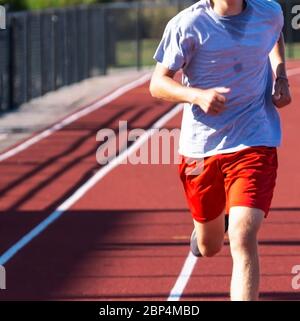 Vista frontale di un corridore di scuola superiore che corre su una pista rossa nella sua corsia di allenamento per pista e campo. Foto Stock