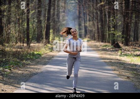 Bella giovane donna in esecuzione nel parco verde sulla soleggiata giornata estiva Foto Stock