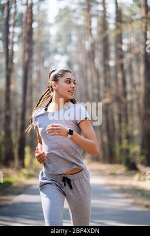 Bella giovane donna in esecuzione nel parco verde sulla soleggiata giornata estiva Foto Stock