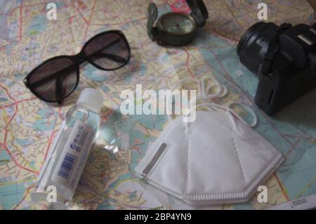 Disposizione piana di un tavolo dove su una mappa vediamo alcune maschere, idrogel per le mani, occhiali, una bussola e una macchina fotografica, gli elementi necessari per ogni turista Foto Stock