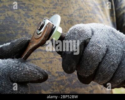 Guanti con mani maschili serrare il dado sul bullone con una chiave Foto Stock