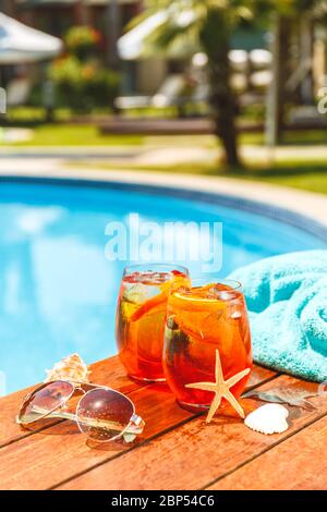 Due bicchieri di aperol Spritz e cocktail negroni con conchiglie, asciugamano e occhiali da sole nel patio estivo vicino alla piscina. Vacanza, estate, vacanza, concetto di resort di lusso. Verticale Foto Stock