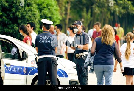 Poliziotti italiani indossando maschere facciali, guardando le persone che si riuniscono nel parco cittadino di Villa Ada a Roma, come misure di allontanamento sociale sono parzialmente attenuati Foto Stock