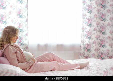 Donna incinta sdraiata sul letto. Guardando lo stomaco, aspettandosi il bambino. Gravidanza, riposo, persone e aspettativa concetto - donna felice incinta sdraiata su b Foto Stock