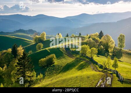 percorso attraverso campi di campagna. bella vista del paesaggio rurale al tramonto. colline che si rotola verso la valle lontana. nuvole sul cielo blu in e. Foto Stock