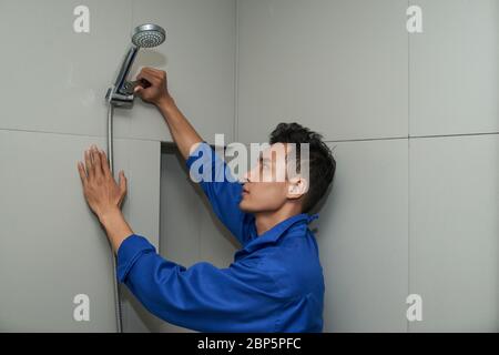 Idraulico in uniforme usando la chiave quando si installa la doccia in bagno Foto Stock