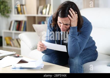 Triste donna adulta che controlla le ricevute seduto nel divano nel soggiorno di casa Foto Stock