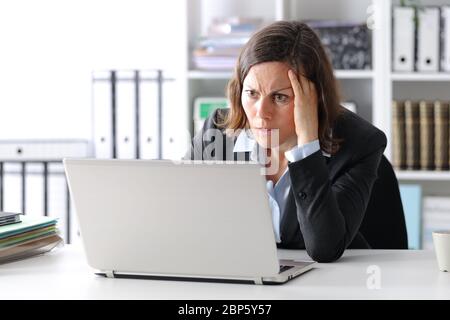 Donna adulta e dirigente preoccupata che legge notizie su un computer portatile seduto su una scrivania in ufficio Foto Stock