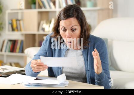 Donna adulta sorpresa che controlla le lettere di ricevuta seduto nel soggiorno a casa Foto Stock