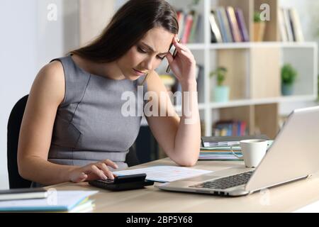 Donna di bookkeeper preoccupata che calcola guardando la calcolatrice seduto su una scrivania a casa Foto Stock