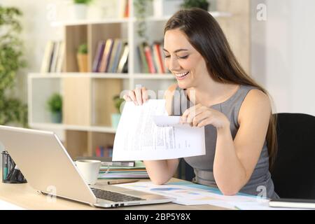 Felice imprenditore donna che infrana il contratto seduto su una scrivania a casa Foto Stock