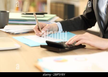 Primo piano di mani del contabile che calcolano l'assegno bancario sulla calcolatrice seduto su una scrivania in ufficio domestico Foto Stock
