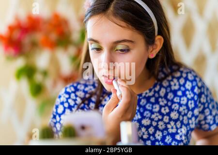 Ragazza giovane attraente che segue un corso di trucco online sul suo smartphone applicando rossetto o lucentezza alle sue labbra in un primo piano ritratto ritagliato Foto Stock