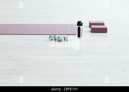 Immagine di sfondo minima del tappetino yoga e delle attrezzature sportive su pavimento in legno bianco in camera vuota, spazio copia Foto Stock