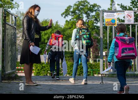 Dresda, Germania. 18 maggio 2020. Costanze Hänsel, direttrice di una scuola elementare, saluta i suoi allievi al mattino all'ingresso della scuola, indossando una guardia alla bocca. Da questo lunedì, le scuole primarie e secondarie riapriranno le loro porte dopo settimane di chiusura forzata a causa della pandemia di Corona. Credit: Robert Michael/dpa-Zentralbild/dpa/Alamy Live News Foto Stock