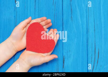 Cuore rosso sulle mani del bambino su sfondo di legno. Concetto medico sanitario. Spazio di copia. Foto Stock