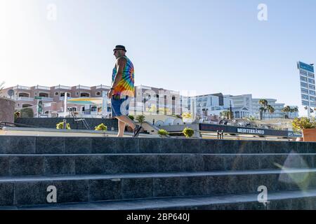 Uomo con un cappello di torta di maiale, barba verde tinta e tie tinta T shirt cammina sulla passeggiata a Playa Fanabe durante la fase uno di de-escalation del Covid 19 Foto Stock